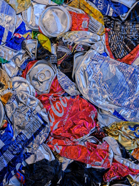 A pile of mixed waste materials accumulated on a gravel surface outdoors, including several black plastic rubbish bags, some partially torn open revealing contents like paper and plastic packaging, an